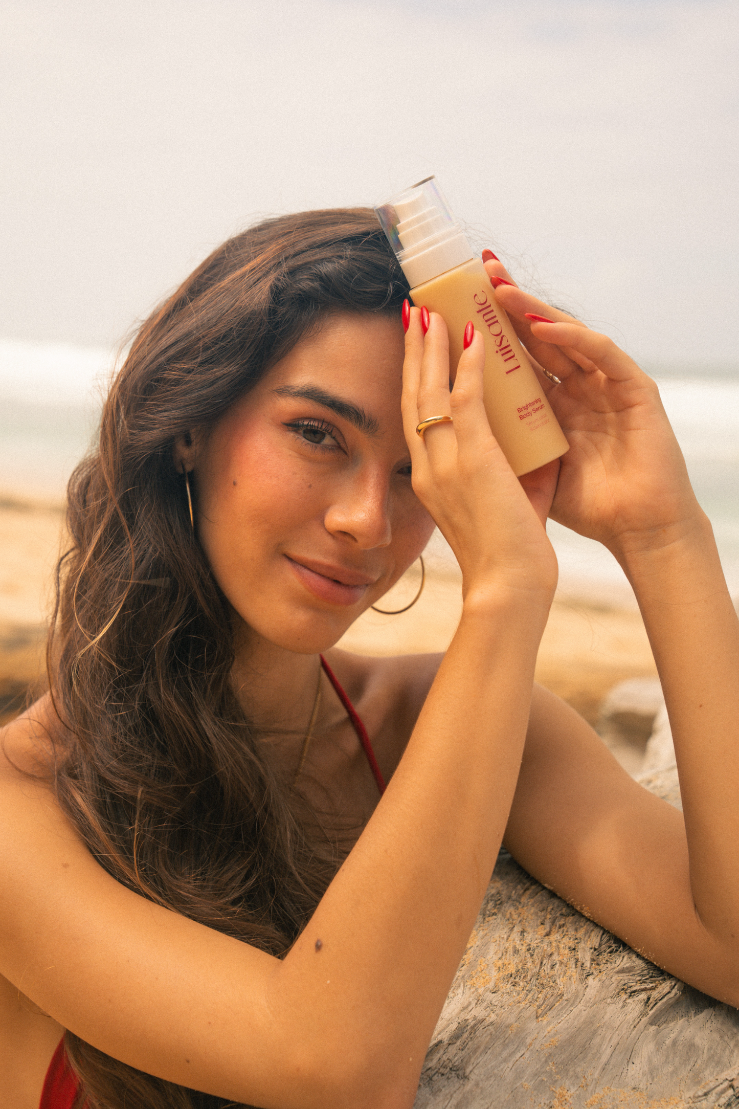 Luisante Brightening Body Serum held by a woman at the beach with waves in the background