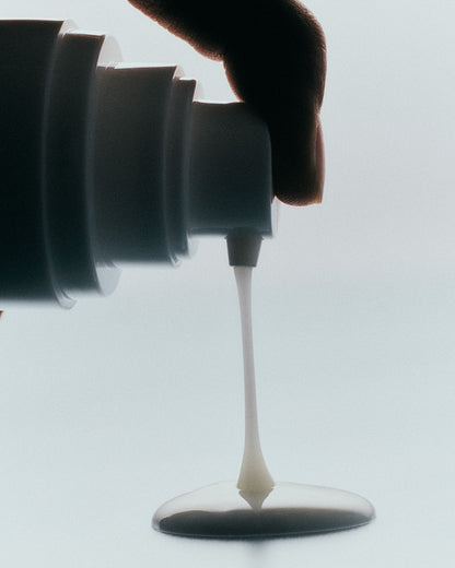Luisante brightening body serum being dispensed from a white pump bottle showing creamy texture
